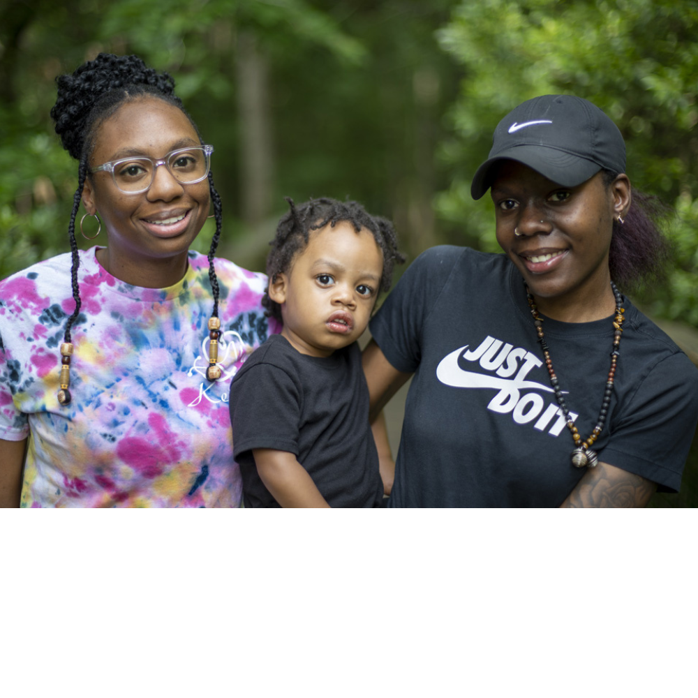 Three black women and a child pose for a photo in the woods.